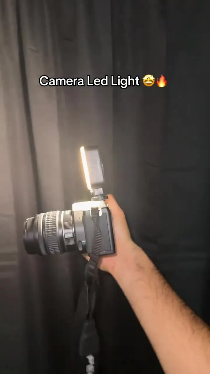 Compact LED light glowing on top of a camera held in front of a dark curtain